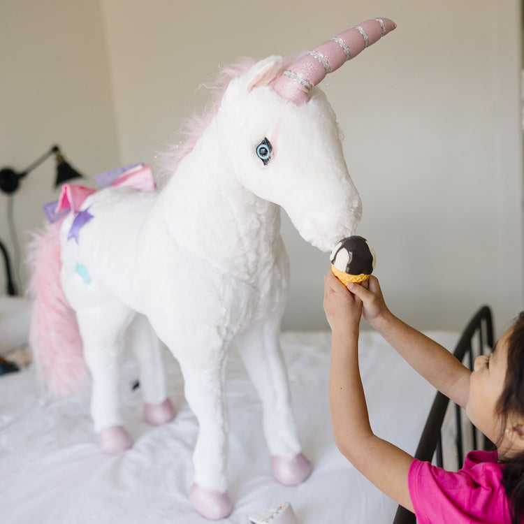 A kid playing with The Melissa & Doug Giant Unicorn - Lifelike Plush Stuffed Animal (over 2 feet tall)