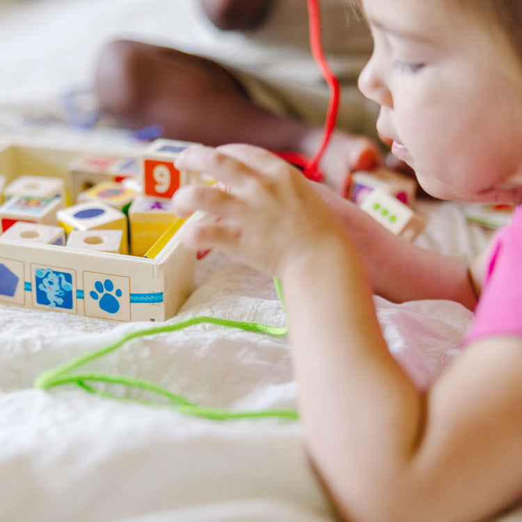 A kid playing with The Melissa & Doug Blue’s Clues & You! Wooden Lacing Beads - 25 Beads, 4 Cords