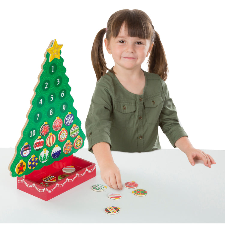 A child on white background with The Melissa & Doug Countdown to Christmas Wooden Advent Calendar - Magnetic Tree, 25 Magnets