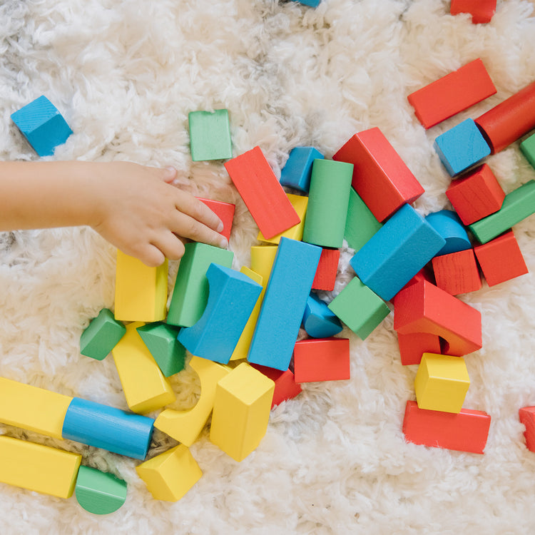 A kid playing with The Melissa & Doug Wooden Building Blocks Set - 100 Blocks in 4 Colors and 9 Shapes