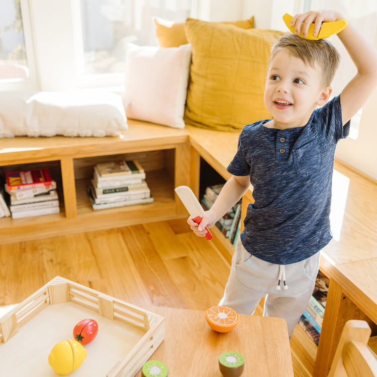 A kid playing with The Melissa & Doug Cutting Fruit Set - Wooden Play Food Kitchen Accessory, Multi