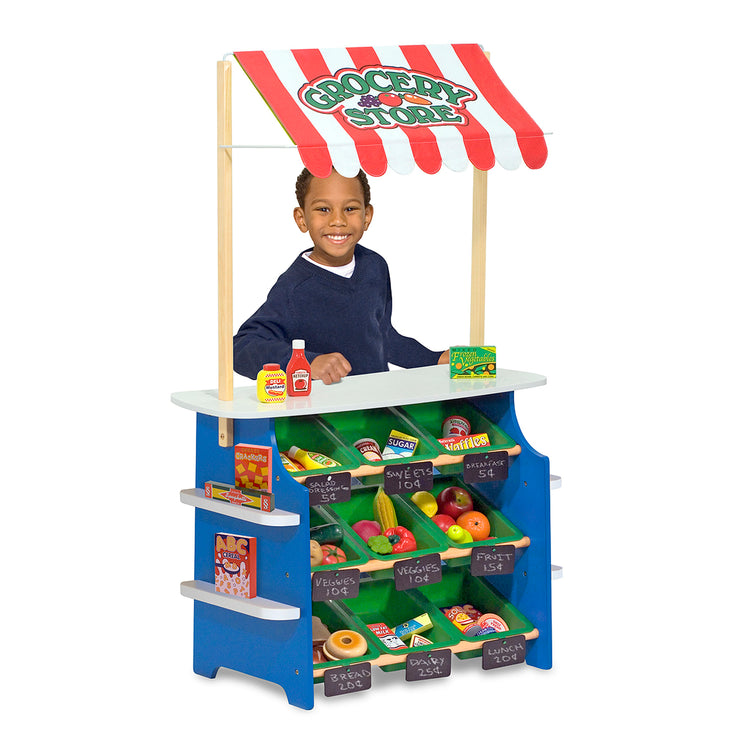 A child on white background with The Melissa & Doug Wooden Grocery Store and Lemonade Stand Activity Center - Reversible Awning, 9 Bins, 9 Chalkboards