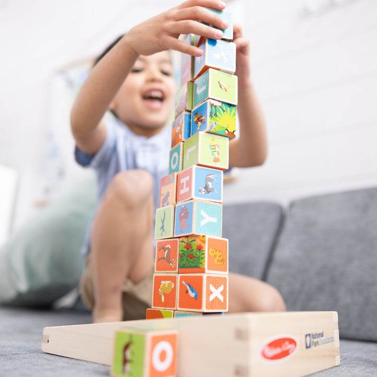 A kid playing with The Melissa & Doug National Parks Alphabet & Animals 24-Piece Cube Puzzle (Everglades, Arches, Yellowstone)