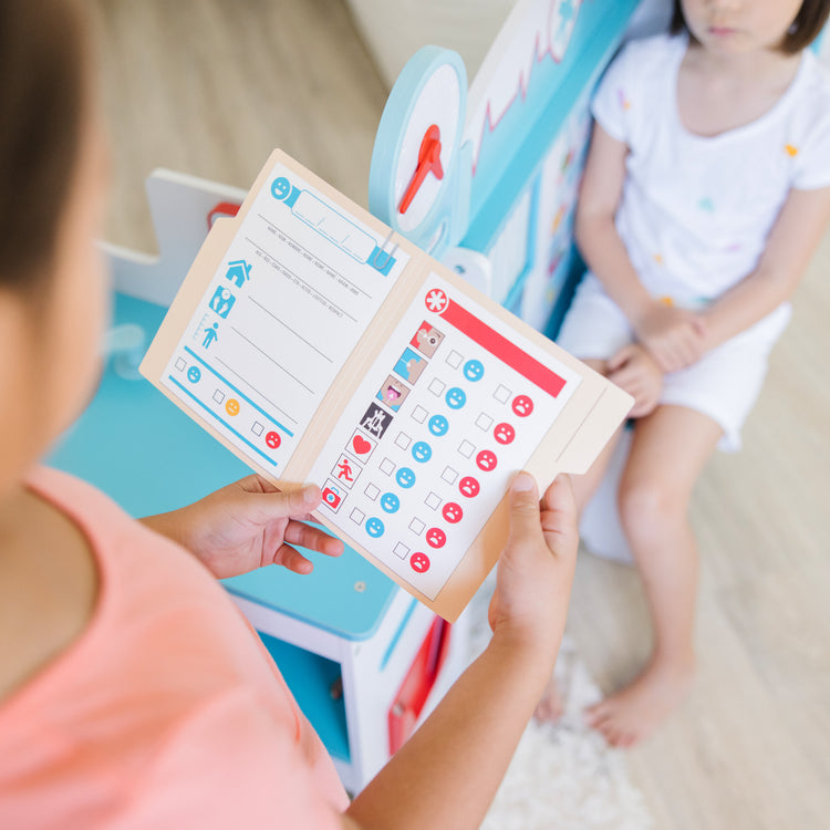 A kid playing with The Melissa & Doug Wooden Get Well Doctor Activity Center - Waiting Room, Exam Room, Check-In Area