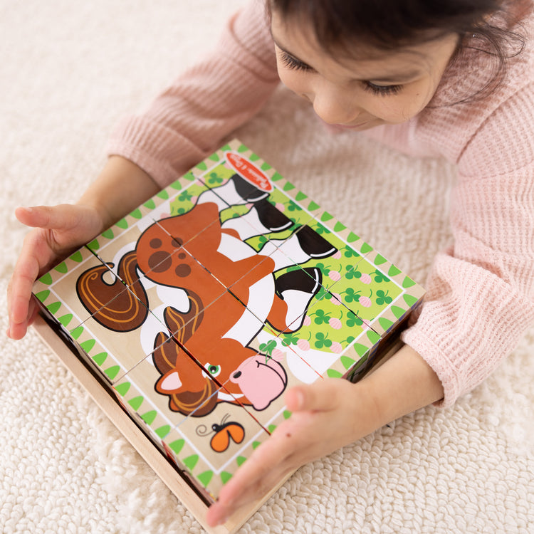 A kid playing with The Melissa & Doug Farm Wooden Cube Puzzle With Storage Tray - 6 Puzzles in 1 (16 pcs)