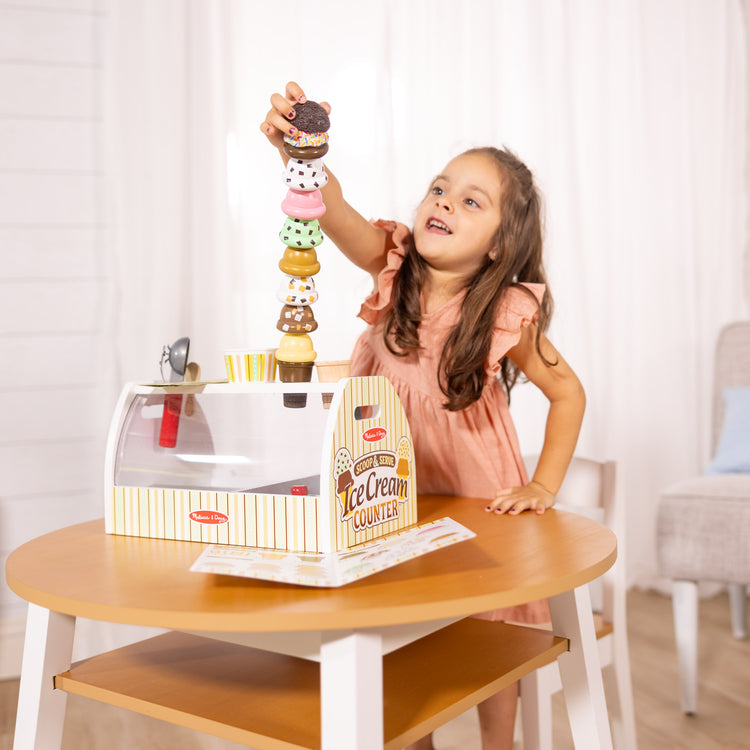 A kid playing with The Melissa & Doug Wooden Scoop and Serve Ice Cream Counter (28 pcs) - Play Food and Accessories