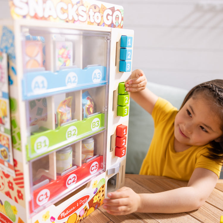 A kid playing with The Melissa & Doug Sort, Stock, Select Wooden Vending Machine Play Set, Wooden Toy Play Food For Boys and For Girls 3+