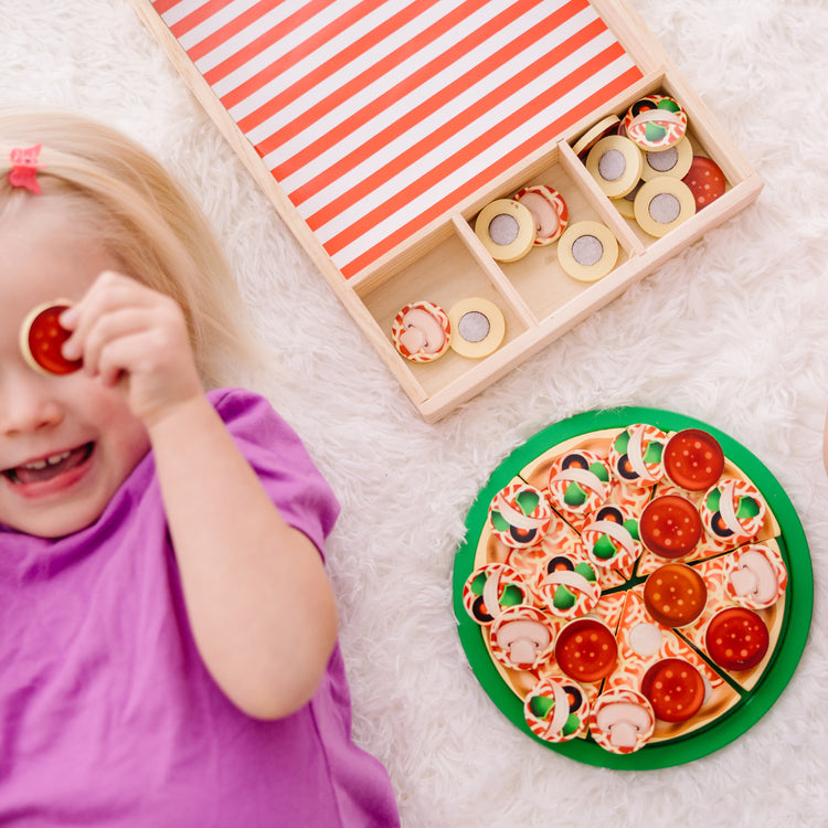 A kid playing with The Melissa & Doug Wooden Pizza Party Play Food Set With 36 Toppings