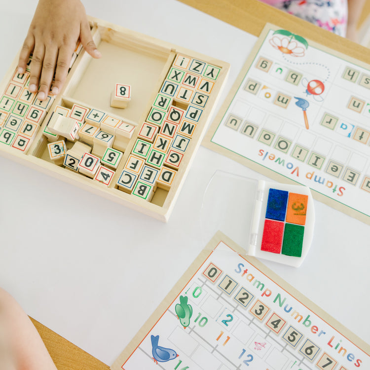 A kid playing with The Melissa & Doug Deluxe Letters and Numbers Wooden Stamp Set ABCs 123s With Activity Book, 4-Color Stamp Pad