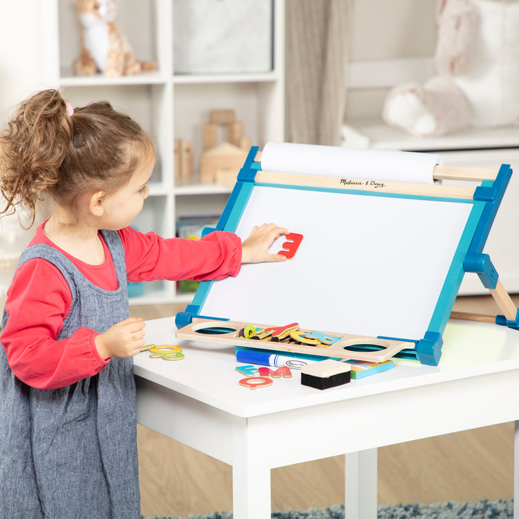 A kid playing with The Melissa & Doug Double-Sided Magnetic Tabletop Art Easel - Dry-Erase Board and Chalkboard