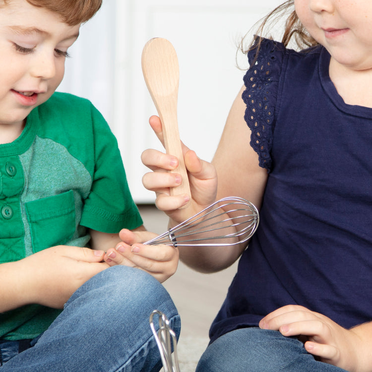 A kid playing with The Melissa & Doug Stir and Serve Cooking Utensils (7 pcs) - Stainless Steel and Wood