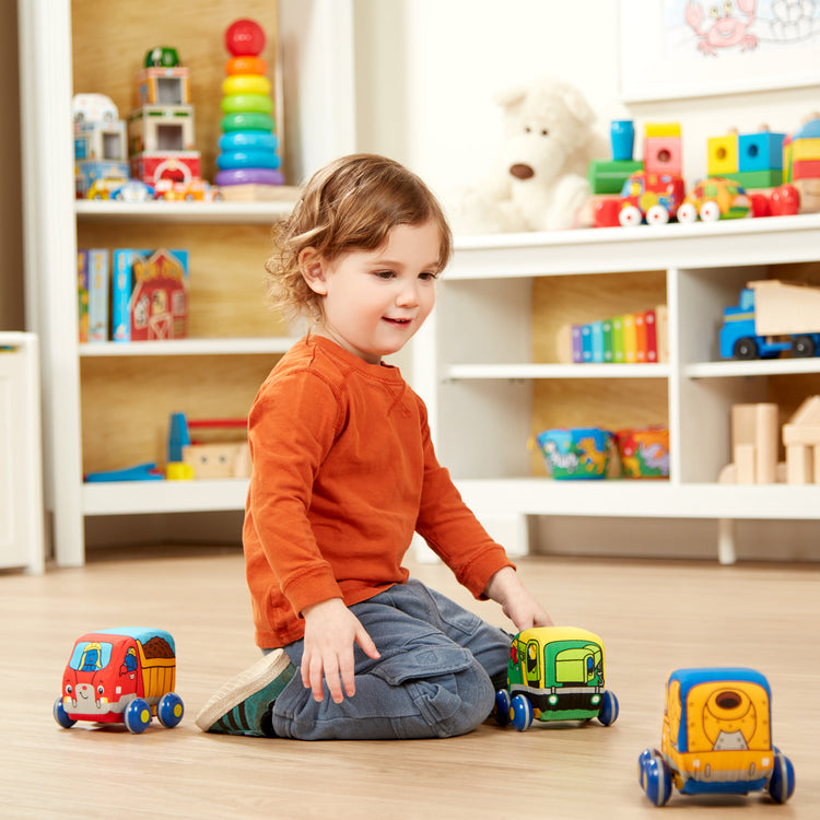 A kid playing with The Melissa & Doug Pull-Back Construction Vehicles - Soft Baby Toy Play Set of 4 Vehicles