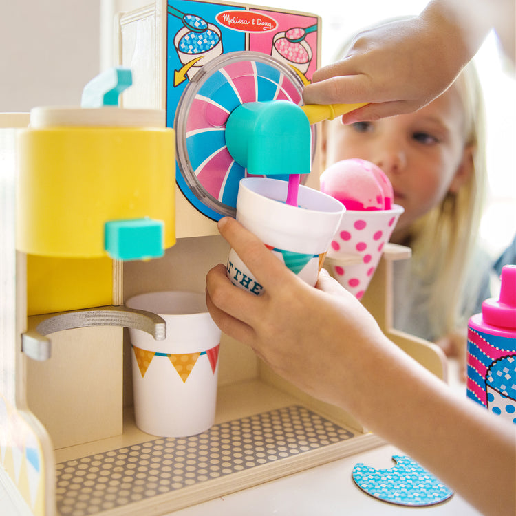 A kid playing with The Melissa & Doug Fun at the Fair! Wooden Snow-Cone and Slushie Play Food Set