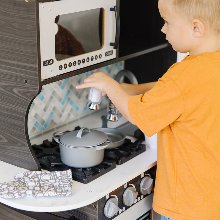 A kid playing with The Melissa & Doug Chef's Wooden Pretend Play Kitchen for Kids With “Ice” Cube Dispenser – Charcoal Gray