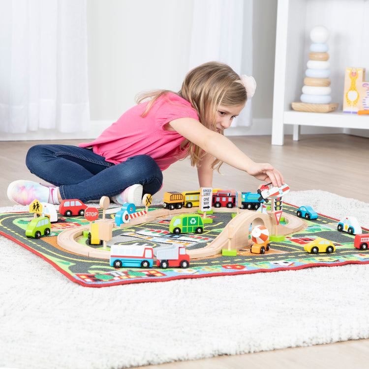 A kid playing with The Melissa & Doug Deluxe Multi-Vehicle Activity Rug (39.5" x 36.5") - 19 Vehicles, 12 Wooden Signs, Train Tracks