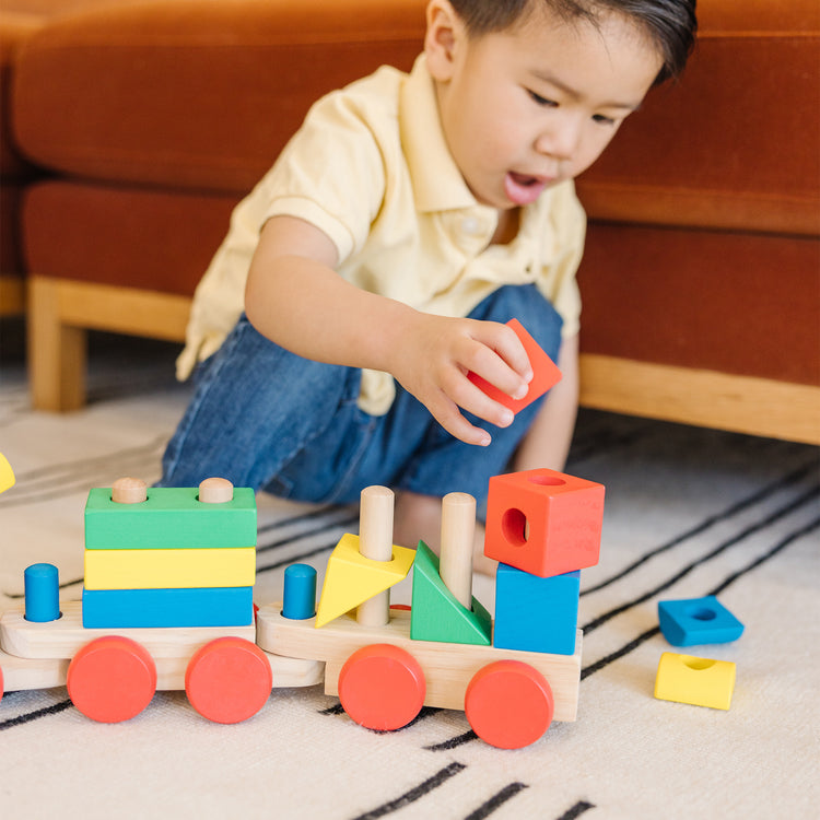 A kid playing with The Melissa & Doug Wooden Stacking Train Learning Toy Vehicle With 18 Connecting Pcs