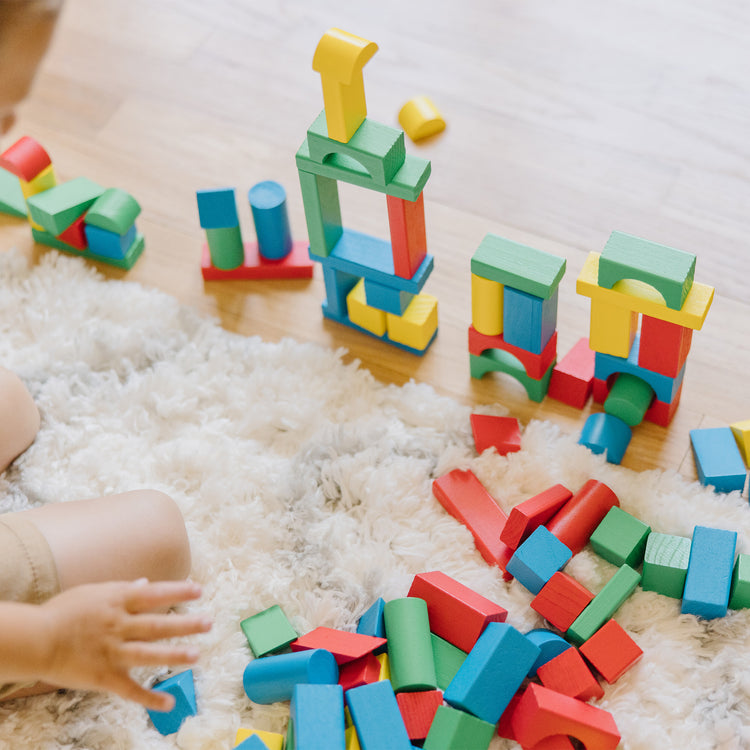 A kid playing with The Melissa & Doug Wooden Building Blocks Set - 100 Blocks in 4 Colors and 9 Shapes