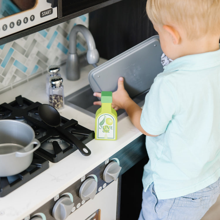 A kid playing with The Melissa & Doug Chef's Wooden Pretend Play Kitchen for Kids With “Ice” Cube Dispenser – Charcoal Gray