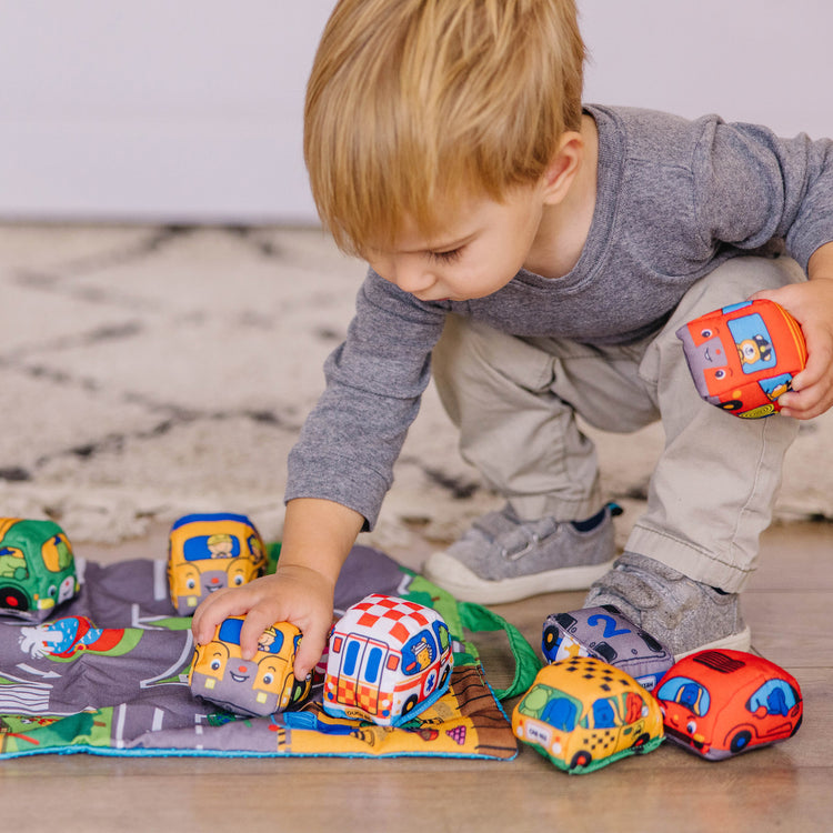 A kid playing with The Melissa & Doug Take-Along Town Play Mat (19.25 x 14.25 inches) With 9 Soft Vehicles