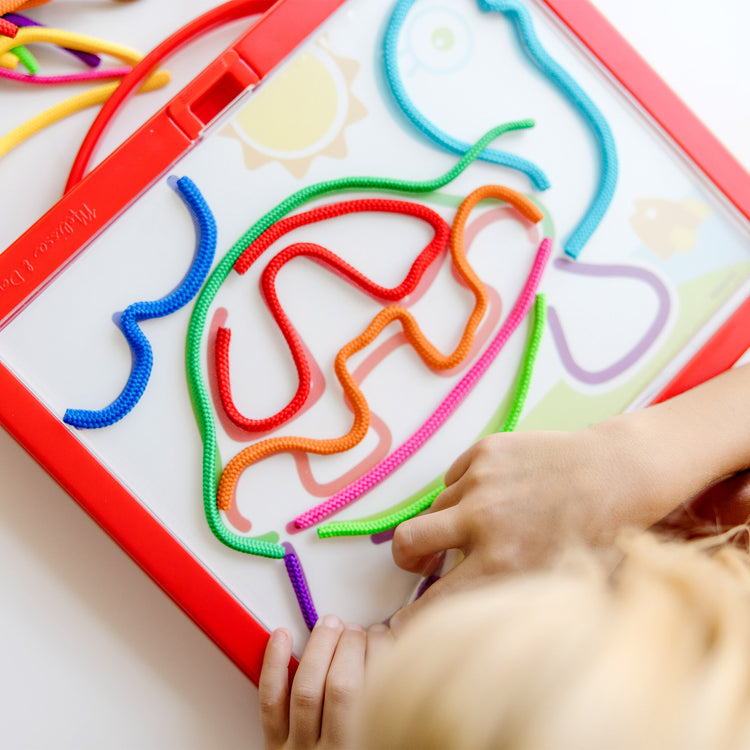 A kid playing with The Melissa & Doug Rainbow Cord Picture And Pattern Maker Draw with Cords Activity – 39 Cords, 6 Double-Sided Cards to Trace