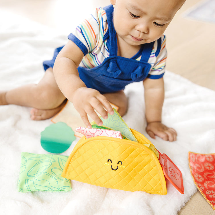 A kid playing with The Melissa & Doug Multi-Sensory Soft Taco Fill & Spill Infant Toy