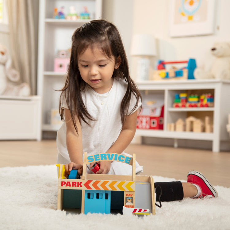 A kid playing with The Melissa & Doug Service Station Parking Garage With 2 Wooden Cars and Drive-Thru Car Wash