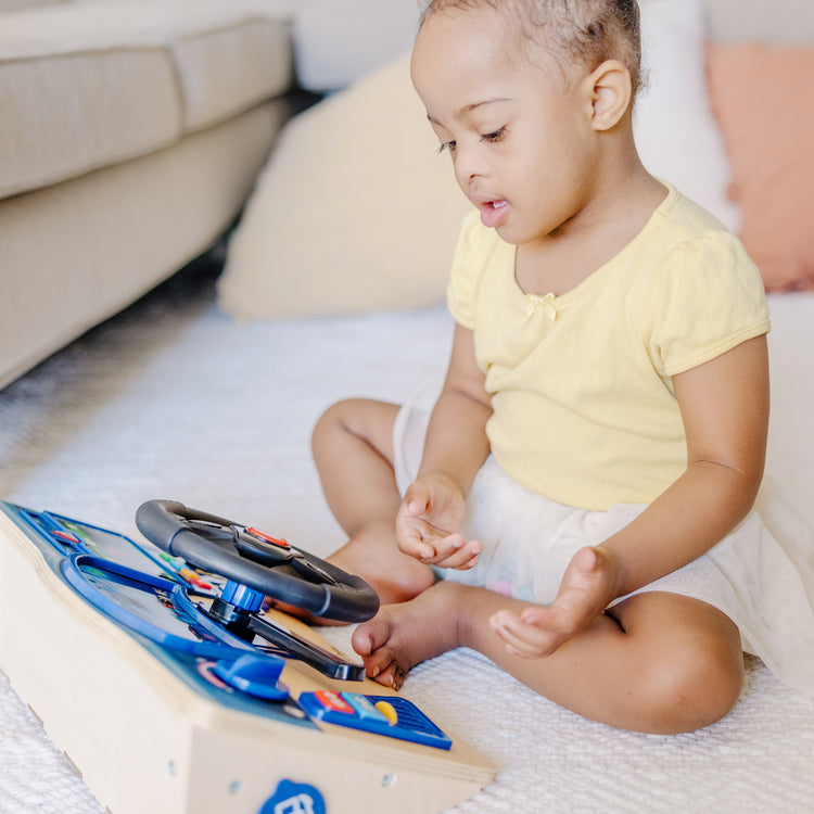 A kid playing with The Melissa & Doug Vroom & Zoom Interactive Wooden Dashboard Steering Wheel Pretend Play Driving Toy