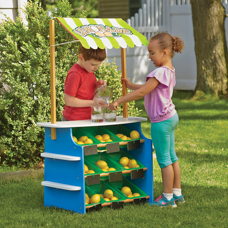 A kid playing with The Melissa & Doug Wooden Grocery Store and Lemonade Stand Activity Center - Reversible Awning, 9 Bins, 9 Chalkboards