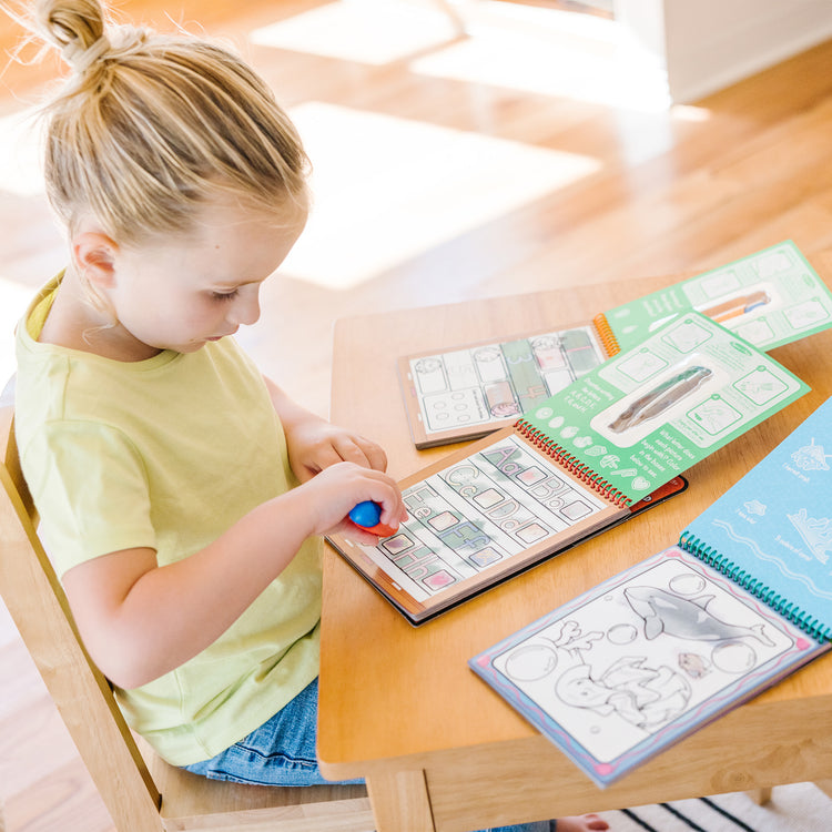 A kid playing with The Melissa & Doug Water Wow! - Water Reveal Pad Bundle - Animals, Alphabet, Numbers and More