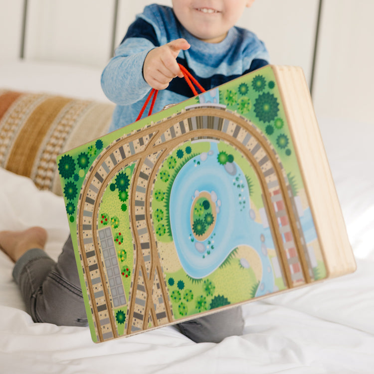 A kid playing with The Melissa & Doug 17-Piece Wooden Take-Along Tabletop Railroad, 3 Trains, Truck, Play Pieces, Bridge