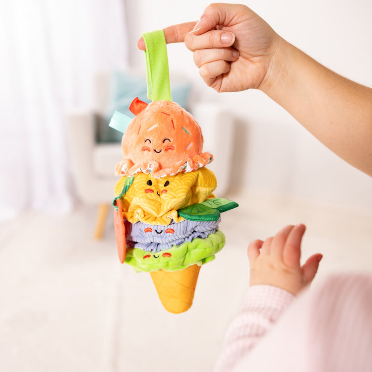 A kid playing with The Melissa & Doug Ice Cream Take-Along Clip-On Infant Toy with Sound and Vibration