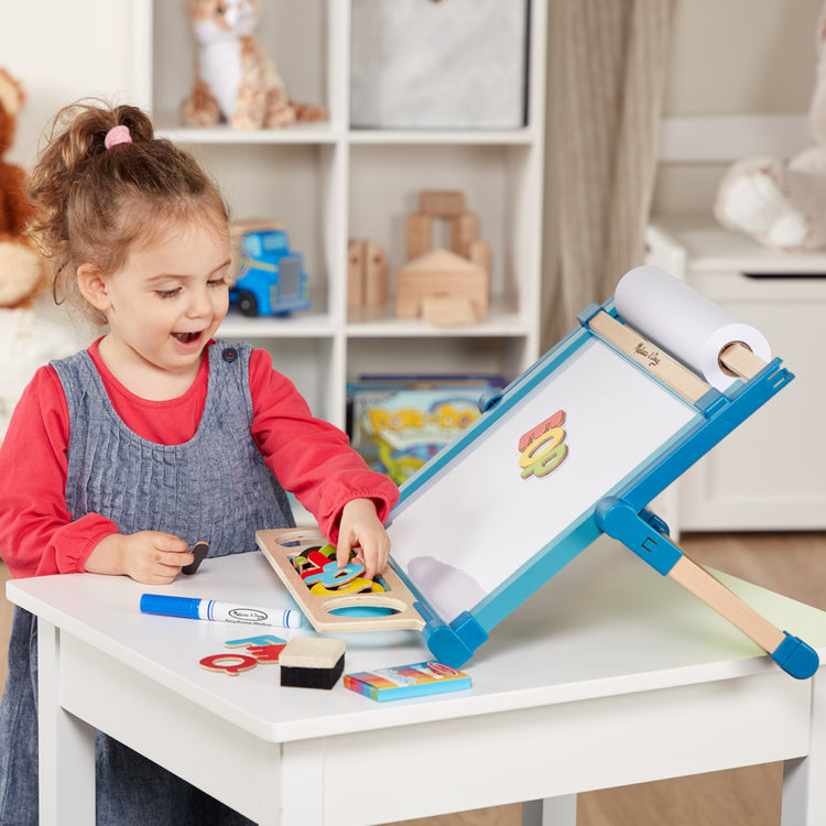 A kid playing with The Melissa & Doug Double-Sided Magnetic Tabletop Art Easel - Dry-Erase Board and Chalkboard