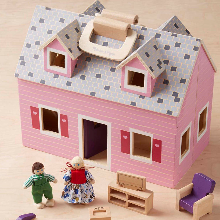 A kid playing with The Melissa & Doug Fold and Go Wooden Dollhouse With 2 Dolls and Wooden Furniture