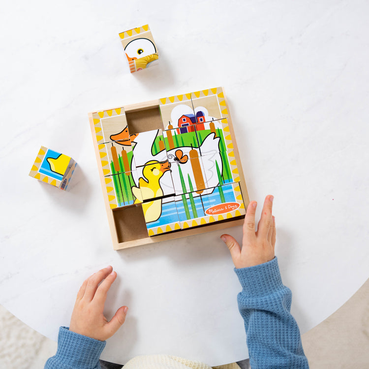 A kid playing with The Melissa & Doug Farm Wooden Cube Puzzle With Storage Tray - 6 Puzzles in 1 (16 pcs)