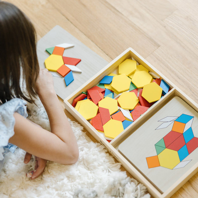 A kid playing with The Melissa & Doug Pattern Blocks and Boards - Classic Toy With 120 Solid Wood Shapes and 5 Double-Sided Panels, Multi-Colored Animals Puzzle