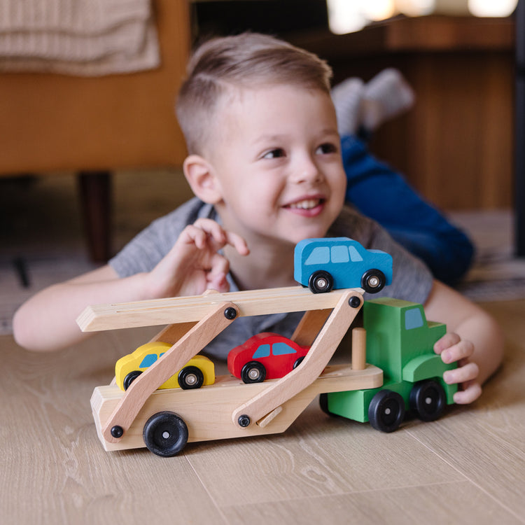 A kid playing with The Melissa & Doug Car Carrier Truck and Cars Wooden Toy Set With 1 Truck and 4 Cars