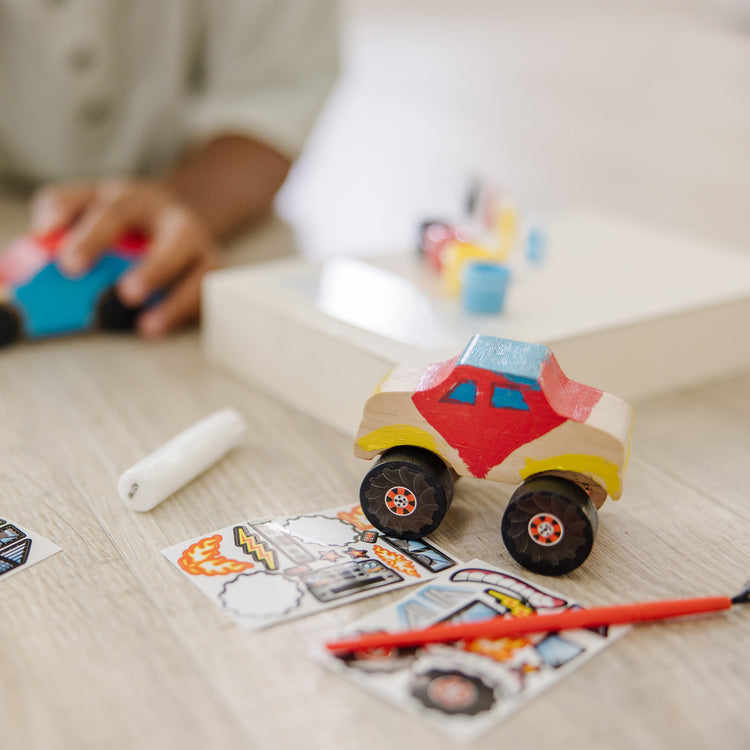 A kid playing with The Melissa & Doug Decorate-Your-Own Wooden Craft Kits Set - Race Car and Monster Truck