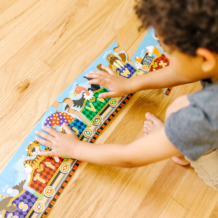 A kid playing with The Melissa & Doug Alphabet Express Jumbo Jigsaw Floor Puzzle (27 pcs, 10 feet long)