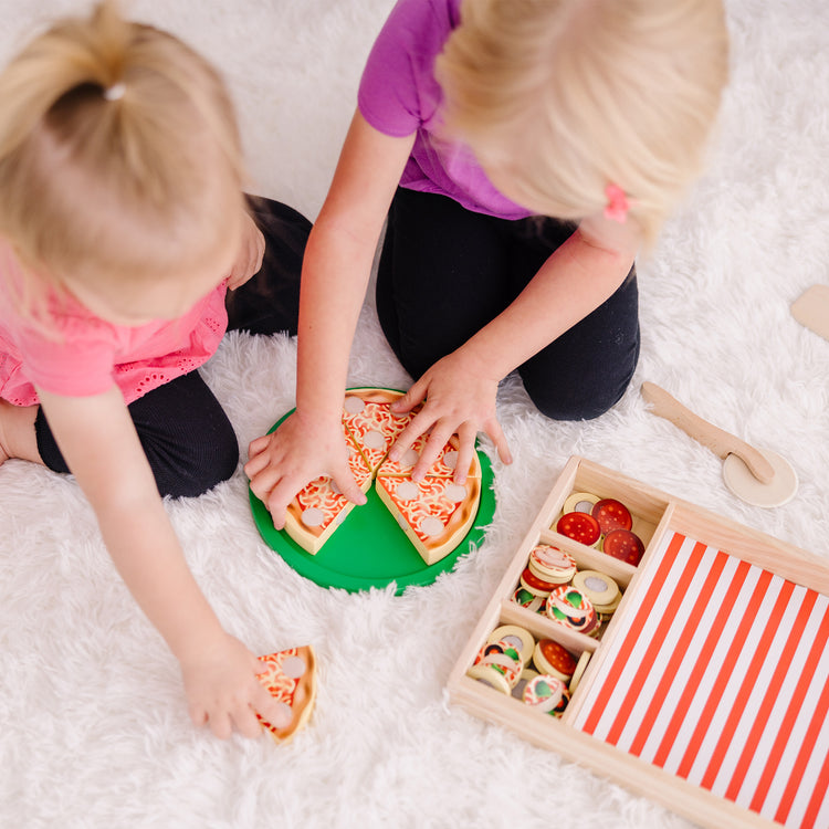 A kid playing with The Melissa & Doug Wooden Pizza Party Play Food Set With 36 Toppings