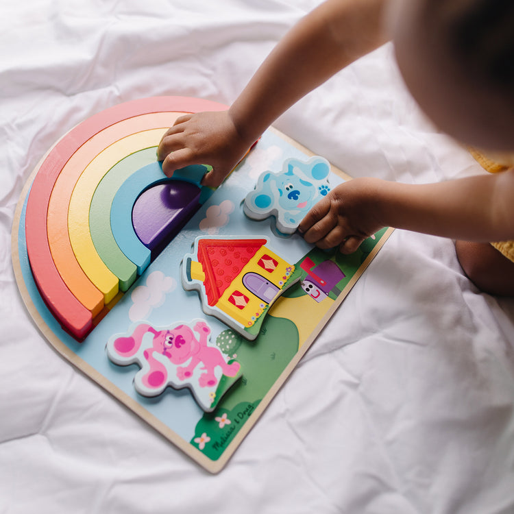 A kid playing with The Melissa & Doug Blue's Clues & You! Wooden Rainbow Stacking Puzzle (9 Pieces)