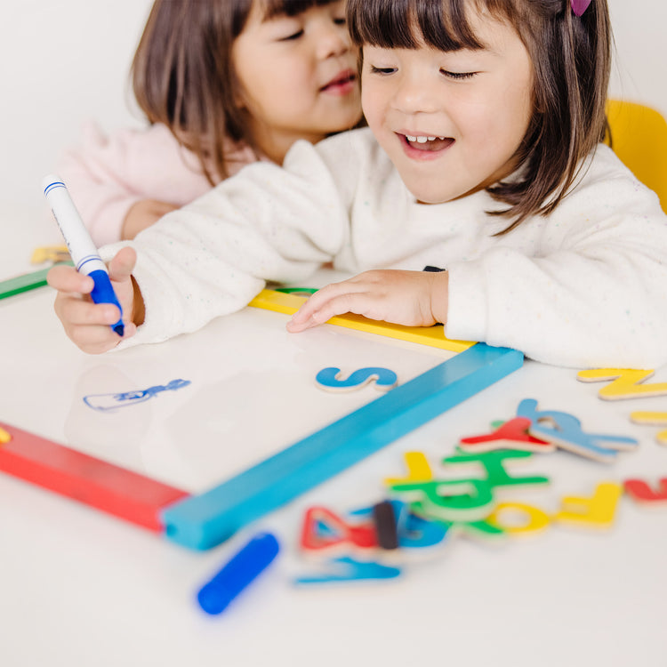 A kid playing with The Melissa & Doug Magnetic Chalkboard and Dry-Erase Board With 36 Magnets (Numbers and Uppercase Letters), Chalk, Eraser, and Dry-Erase Pen