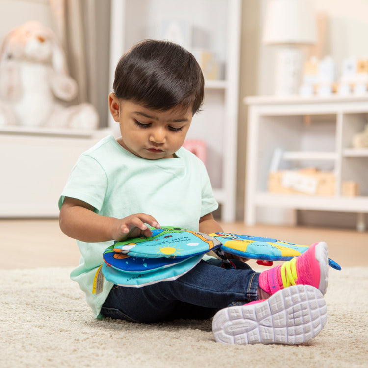 A kid playing with The Melissa & Doug K's Kids Itsy-Bitsy Spider 8-Page Soft Activity Book for Babies and Toddlers