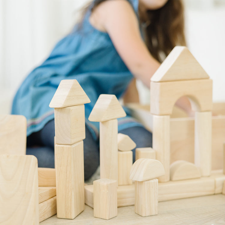 A kid playing with The Melissa & Doug Standard Unit Solid-Wood Building Blocks With Wooden Storage Tray (60 pcs)