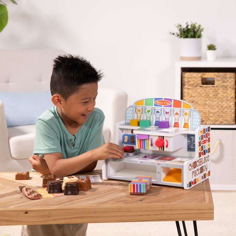 A kid playing with The Melissa & Doug Wooden Chocolate Factory Pretend Play Set, Play Food Candy Maker for Boys and Girls