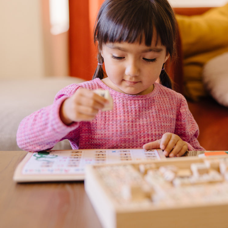 A kid playing with The Melissa & Doug Deluxe Letters and Numbers Wooden Stamp Set ABCs 123s With Activity Book, 4-Color Stamp Pad