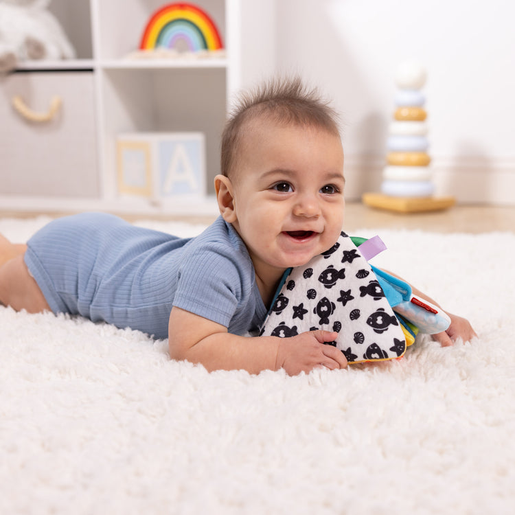 A kid playing with The Melissa & Doug Ocean Tummy Time Triangle Infant Baby Toy, Soft Sensory Toy with Textures, Mirror, Floor Toy for Newborns to Ages 6 Months