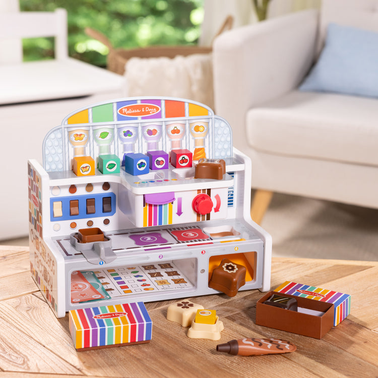 A kid playing with The Melissa & Doug Wooden Chocolate Factory Pretend Play Set, Play Food Candy Maker for Boys and Girls