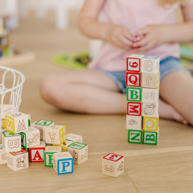 A kid playing with The Melissa & Doug Deluxe Wooden ABC/123 1-Inch Blocks Set With Storage Pouch (50 pcs)