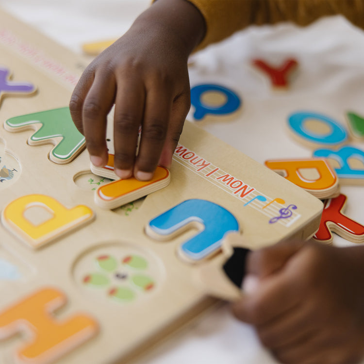 A kid playing with The Melissa & Doug Wooden Alphabet Sound Puzzle - Wooden Puzzle With Sound Effects (26 pcs)