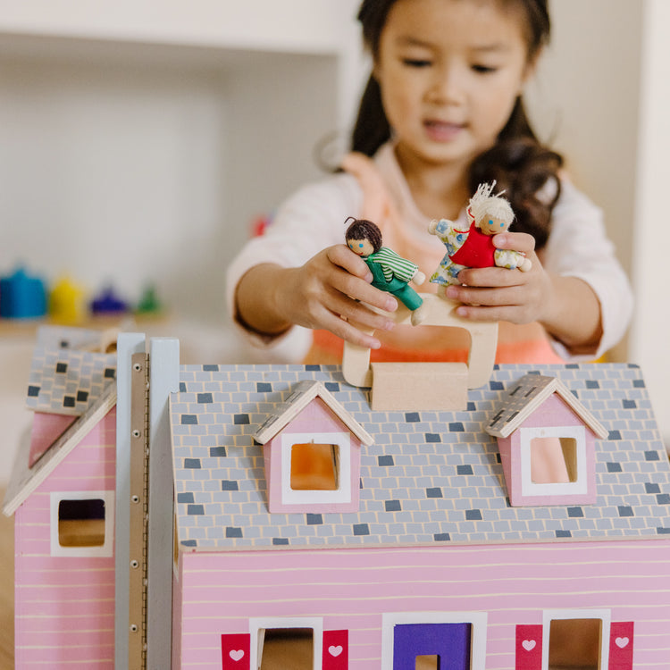 A kid playing with The Melissa & Doug Fold and Go Wooden Dollhouse With 2 Dolls and Wooden Furniture